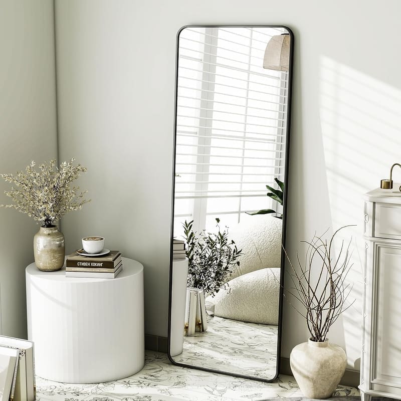 The Artment Vista 155 × 45 cm arched full-length floor mirror in black aluminium frame, leaning against a bedroom wall with the full reflection of a styled corner visible